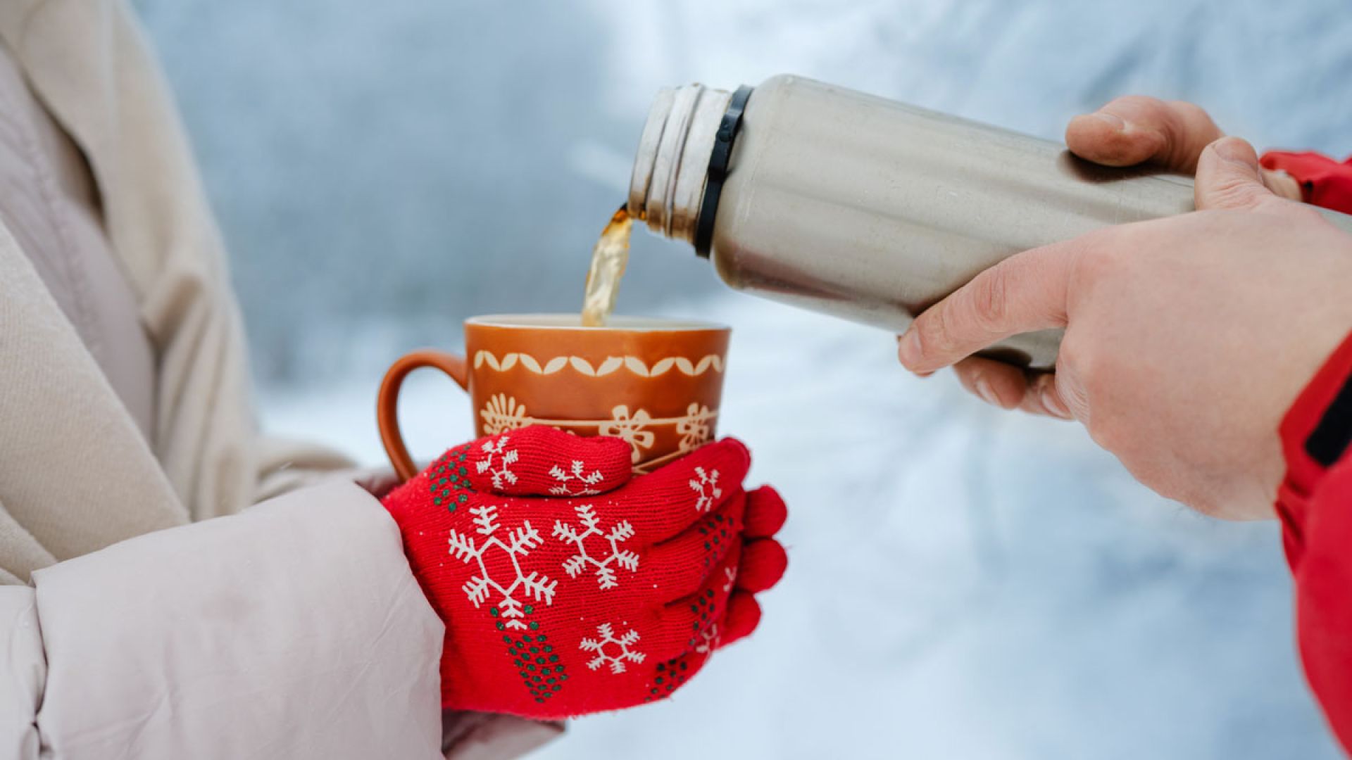 person pouring hot beverage for another person in winter weather